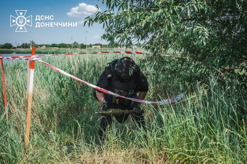 Мужній працівник ДСНС обережно несе снаряд на спеціальне місце. Чоловік міцної статури у засобах захисту.