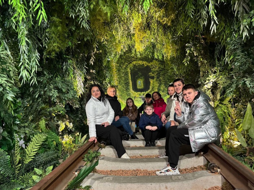 Діти сидять на рельсах, з обох боків зелені дерева.