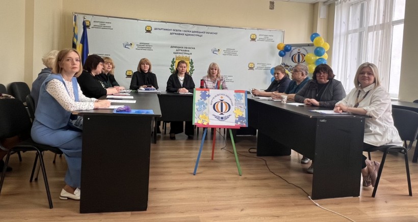 Учасники Форуму освітніх інновацій–2025 за круглим столом. На передньому плані стенд із логотипом події та пазлами