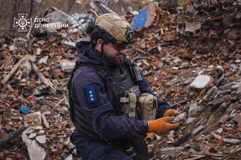 Піротехник ДСНС,стоїть на місці обстрілу, тримає в руках уламок від вибухонебезпечного предмету.