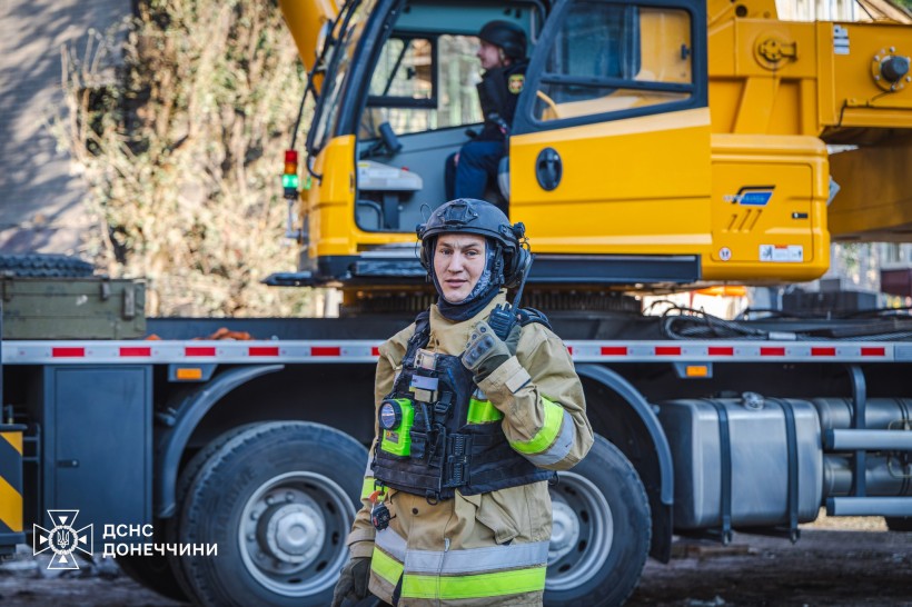 Рятувальник з ліхтарем на бронежилеті, позаду техніка для розбору завалів.