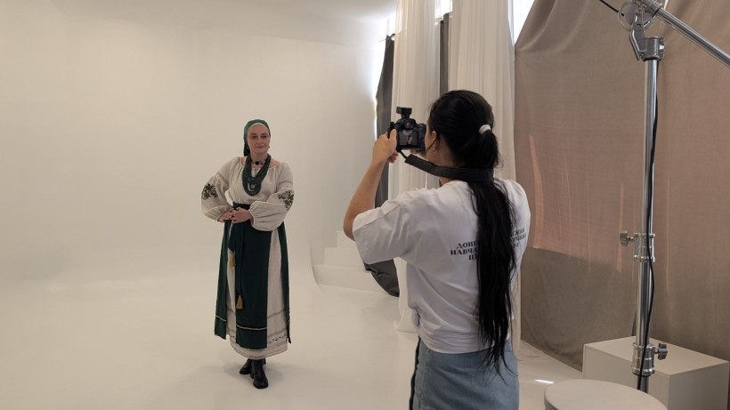 Жінка в традиційному українському костюмі з намистом позує для фотографині у студії