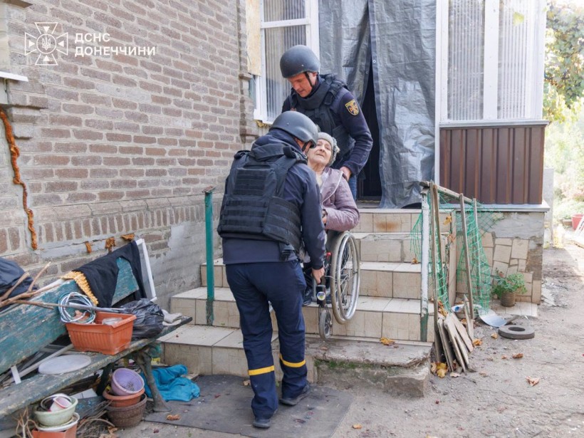 Рятувальники виносять з будинку жінку на кріслі колісному