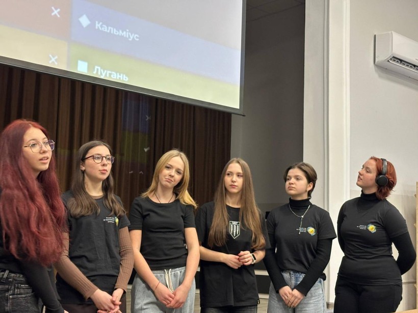 Дівчата у чорних футболках, беруть участь у вікторині. Позаду лед-екран з запитаннями.