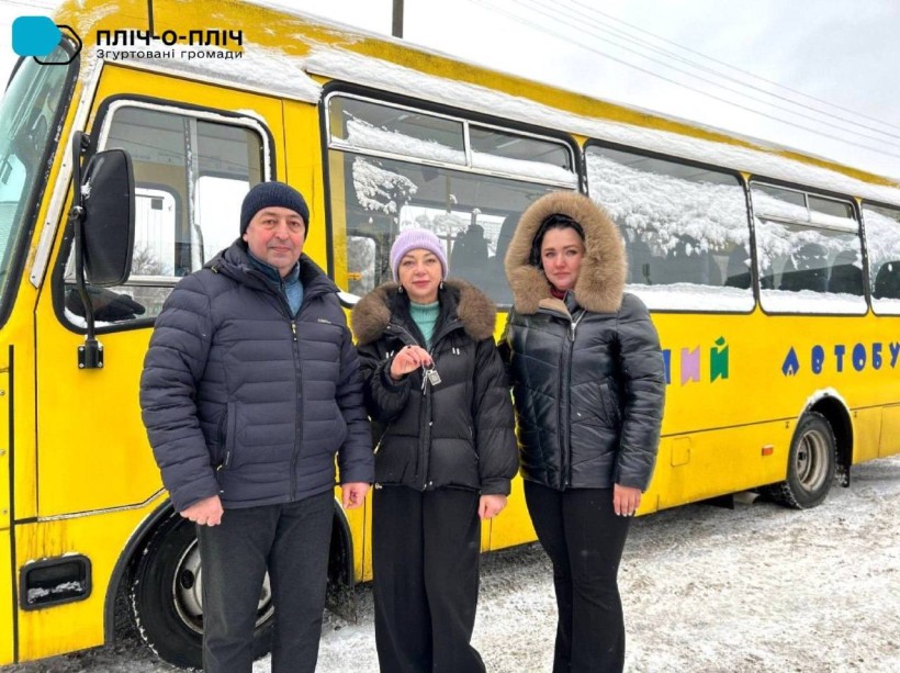 Поруч з автобусом селищний голова Ружинської громади тримає ключі від шкільного автобуса, поруч стоять представники Торецької МВА