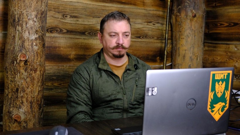 Роман Балабойко сидить за столом і дивиться у монітор ноутбука із шевроном «Щит».