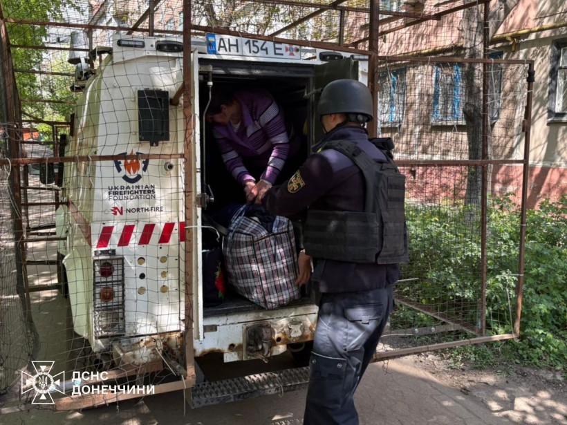 Рятувальники допомагають літній жінці сісти в евакуаційний автомобіль