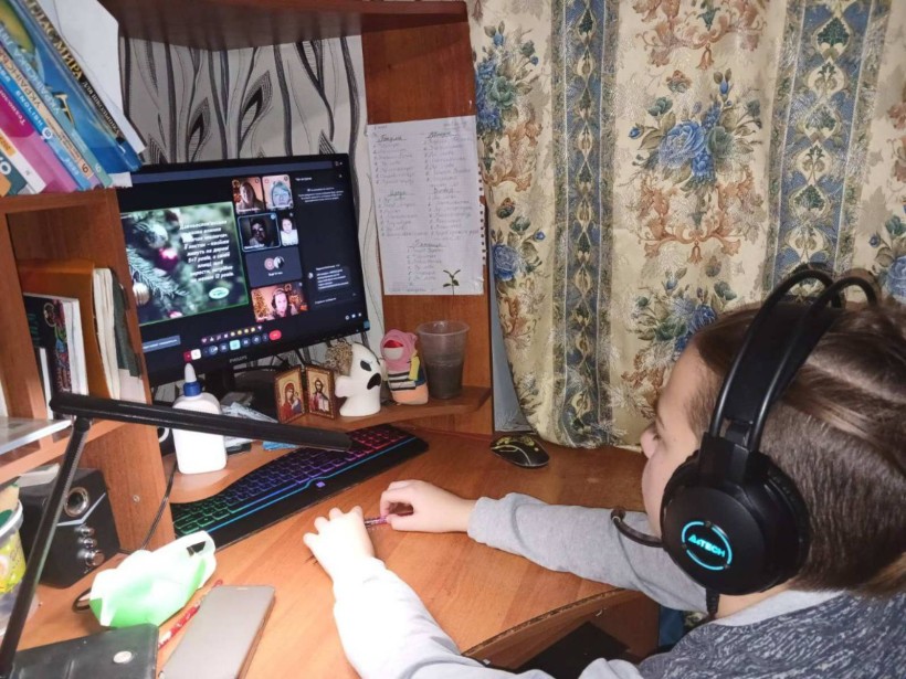 Хлопчик сидить перед комп'ютером та бере участь в онлайновому засіданні Академії юних дослідників