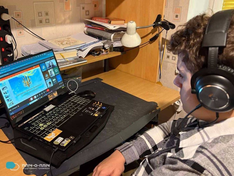 Учень сидить біля екрану монітора у навушниках.