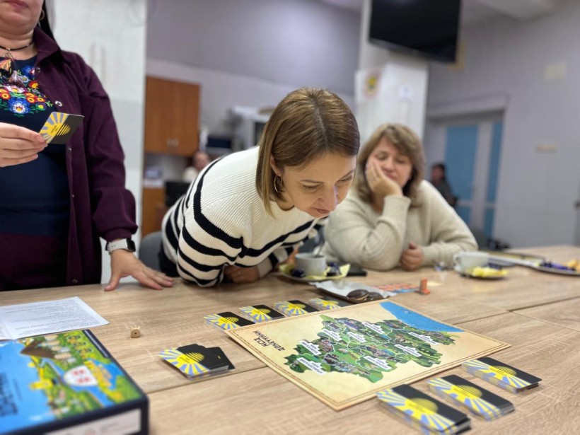 Жінка уважно розглядає настільну гру проДонеччину. На столі лежить гра та картки з логотипом.