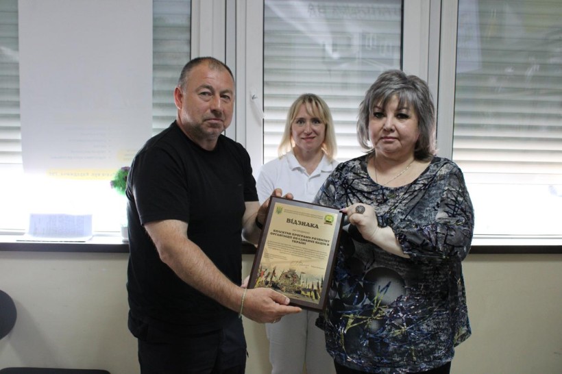 Директор департаменту соціального захисту населення Олена Токарева нагороджує колектив ПРООН в Україні відзнакою від Донецької облдержадміністрації, та передає її начальнику Сартанської селищної військової адміністрації Олександр Куркчи