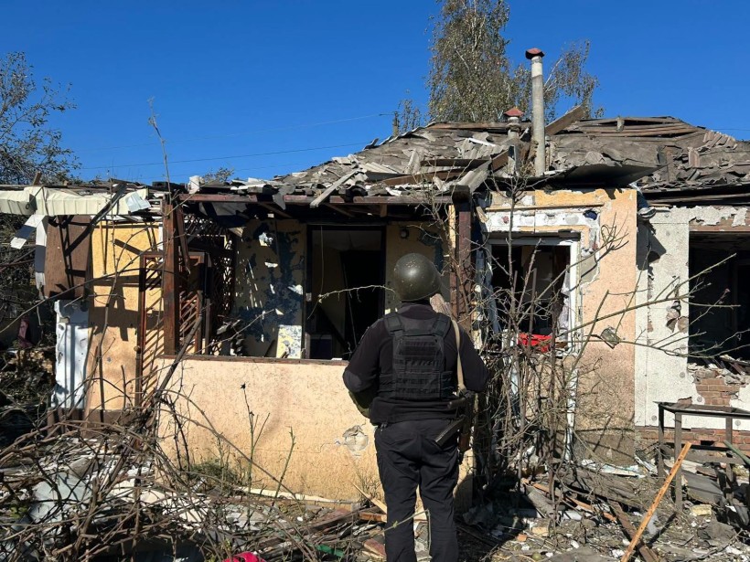 Зруйновані будинки після ворожого обстрілу та правоохоронець, який стоїть поруч з ними
