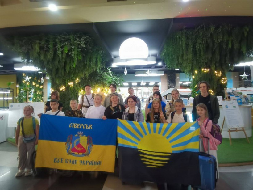 Дівчата та хлопці з Сіверської громади тримають прапори Донеччини та Сіверської громади. Позаду велика біла куля, яка світиться.
