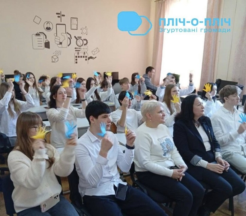 Учасники заходу сидять на стільцях та в руках тримають блакитні та жовті картки.