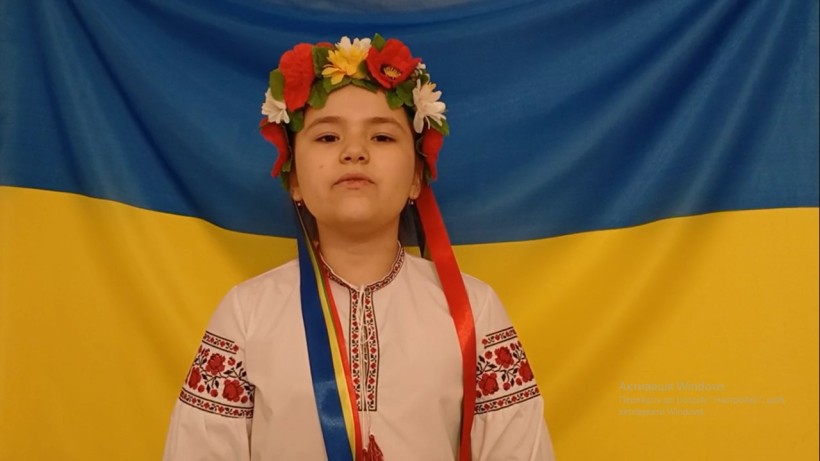 Учасниця конкурсу в українському національному вбранні читає вірш на тлі державного прапора України