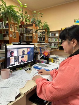 Жінка сидить у бібліотеці та бере участь в онлайновій зустрічі