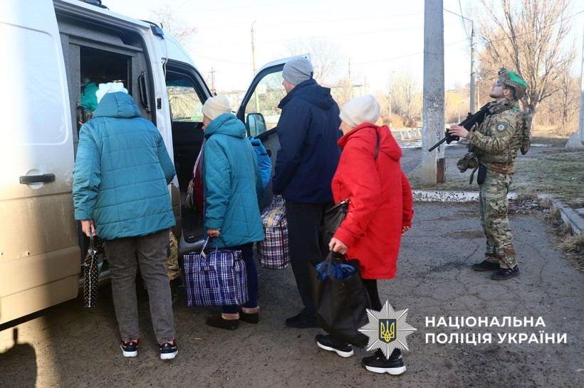 Літні люди сідають до евакомобіля, а поліцейський стежить за небом