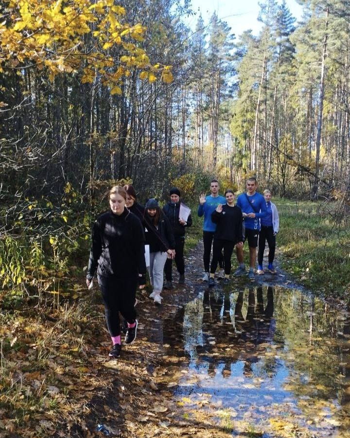 Спортсмени ідуть стежкою у лісі, навкруги дерева. Всі одягнути у спортивні костюми.