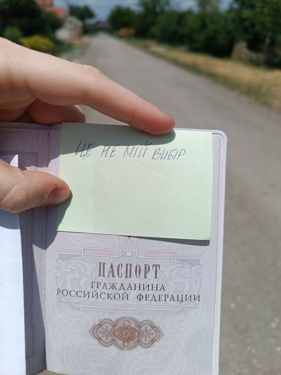 Чоловіча рука тримає паспорт Росії та записку українською мовою в підтримку акції.