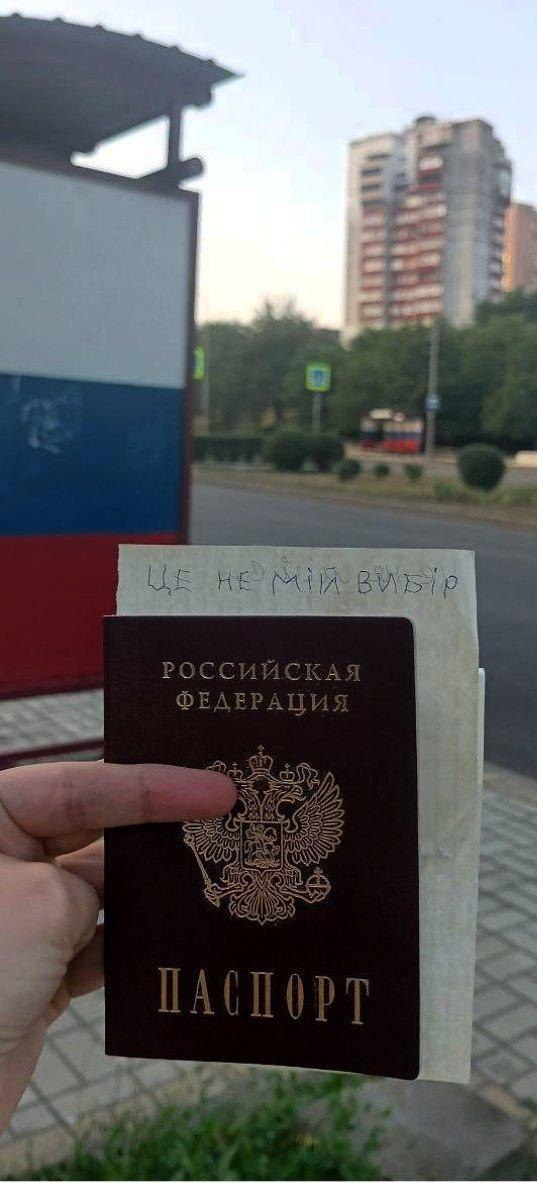 Зупинка громадського транспорту розмальована в кольорах РФ. Рука тримає паспорт РФ з патріотичною запискою у підтримку України.
