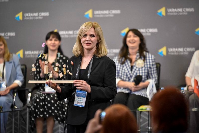 Учасниця STEM-форуму тримає нагороду, позаду — панельна дискусія на тлі логотипів Ukraine Crisis Media Center