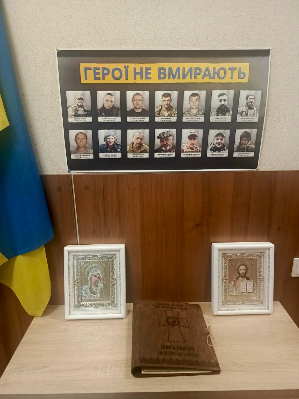 Стенд із портретами загиблих військовослужбовців з написом «Герої не вмирають». Поруч — ікони та книга у дерев’яній обкладинці.