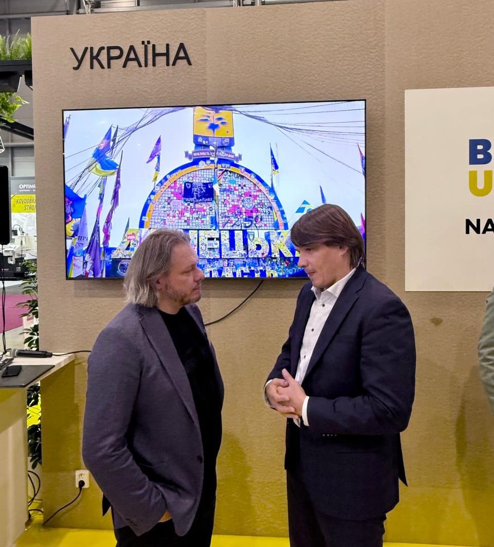 Учасники форму, спілкуються біля екрану на якому стела Донеччини.