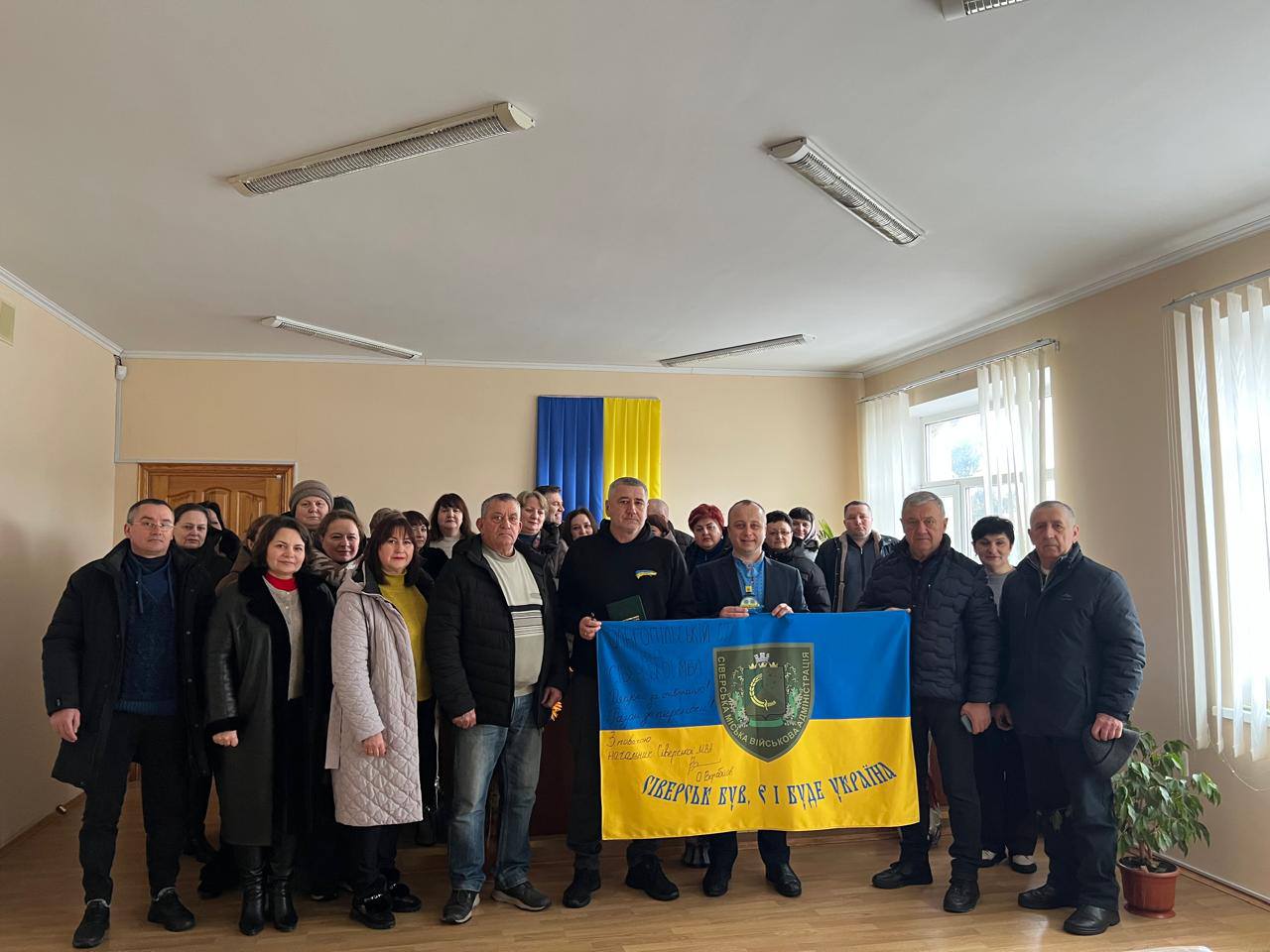 Спільне фото учасників робочої зустрічі. Начальник Сіверської міської військової адміністрації Донецької області Олексій Воробйов тримає попереду прапор громади.