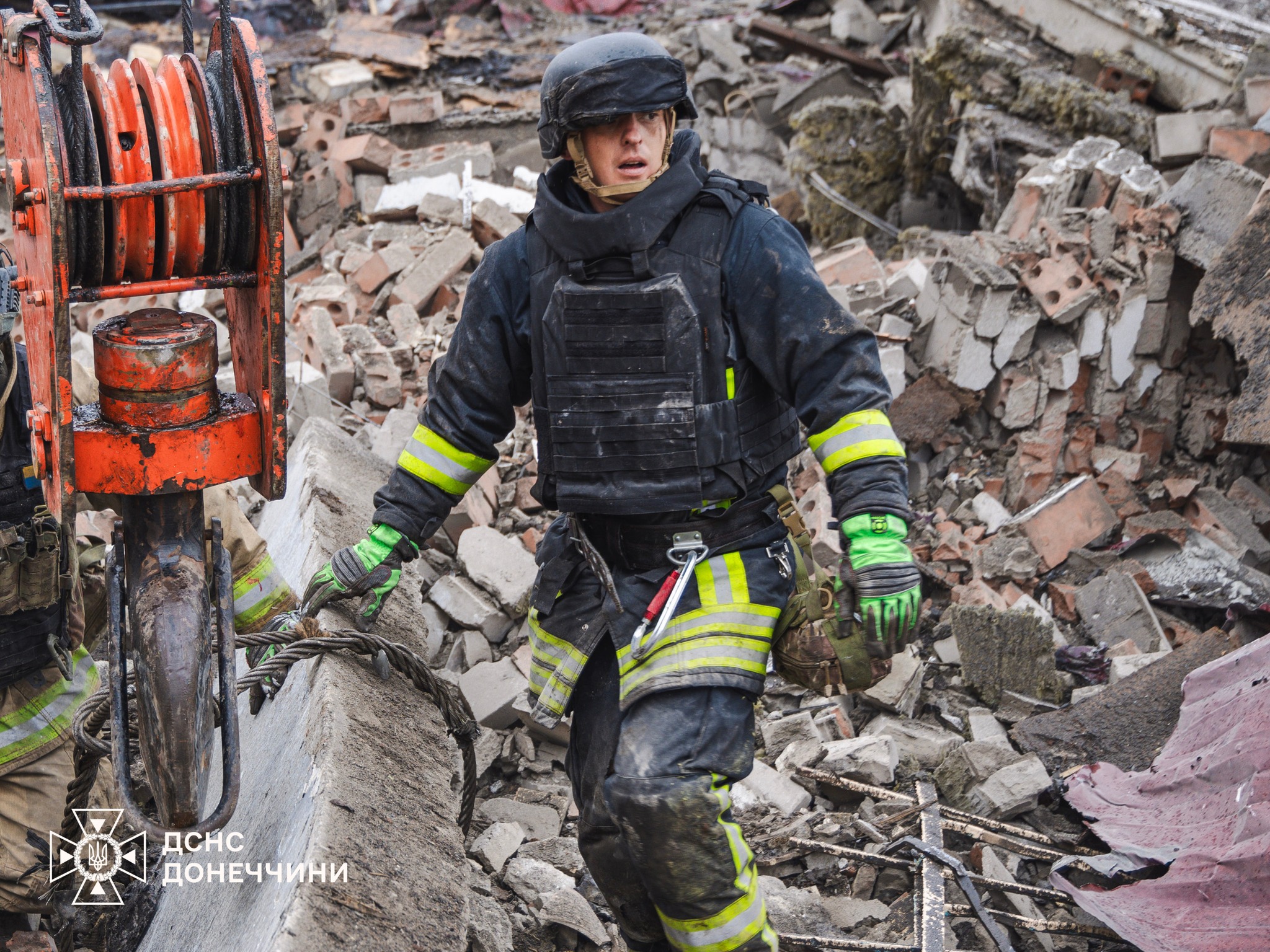 Рятувальник йде до спеціального автомобіля, навкруги каміння після обстрілу.