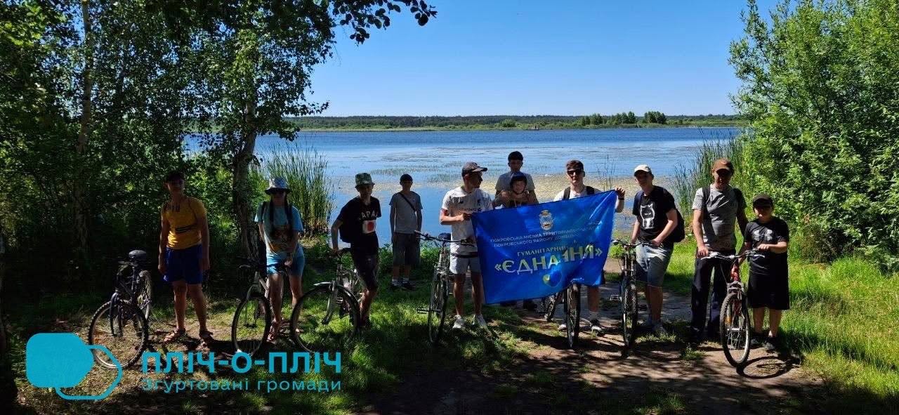 Велосипедисти на березі водойми тримають прапор хабу "Єднання"