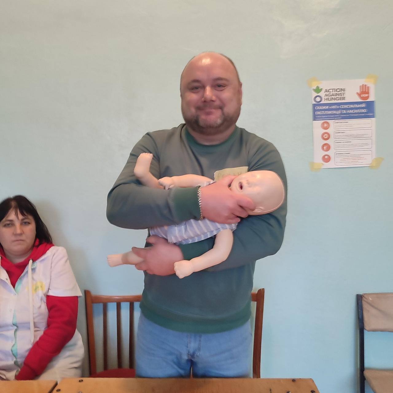 Чоловік тримає манекен немовля.